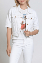Person wearing a white denim jacket over a graphic t-shirt and white pants on a plain background