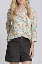 Woman wearing a floral blouse and black shorts on a plain background