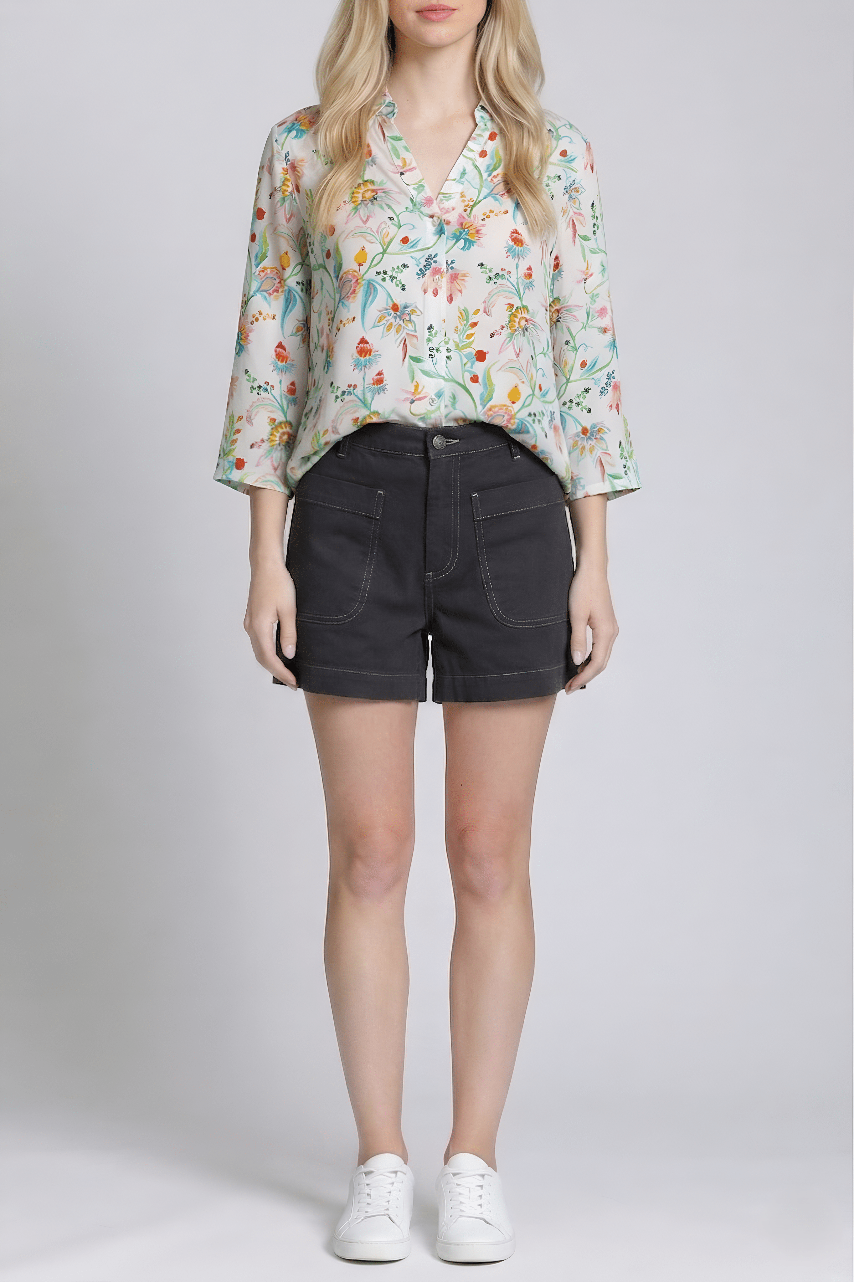 Woman wearing a floral blouse and black shorts on a plain background