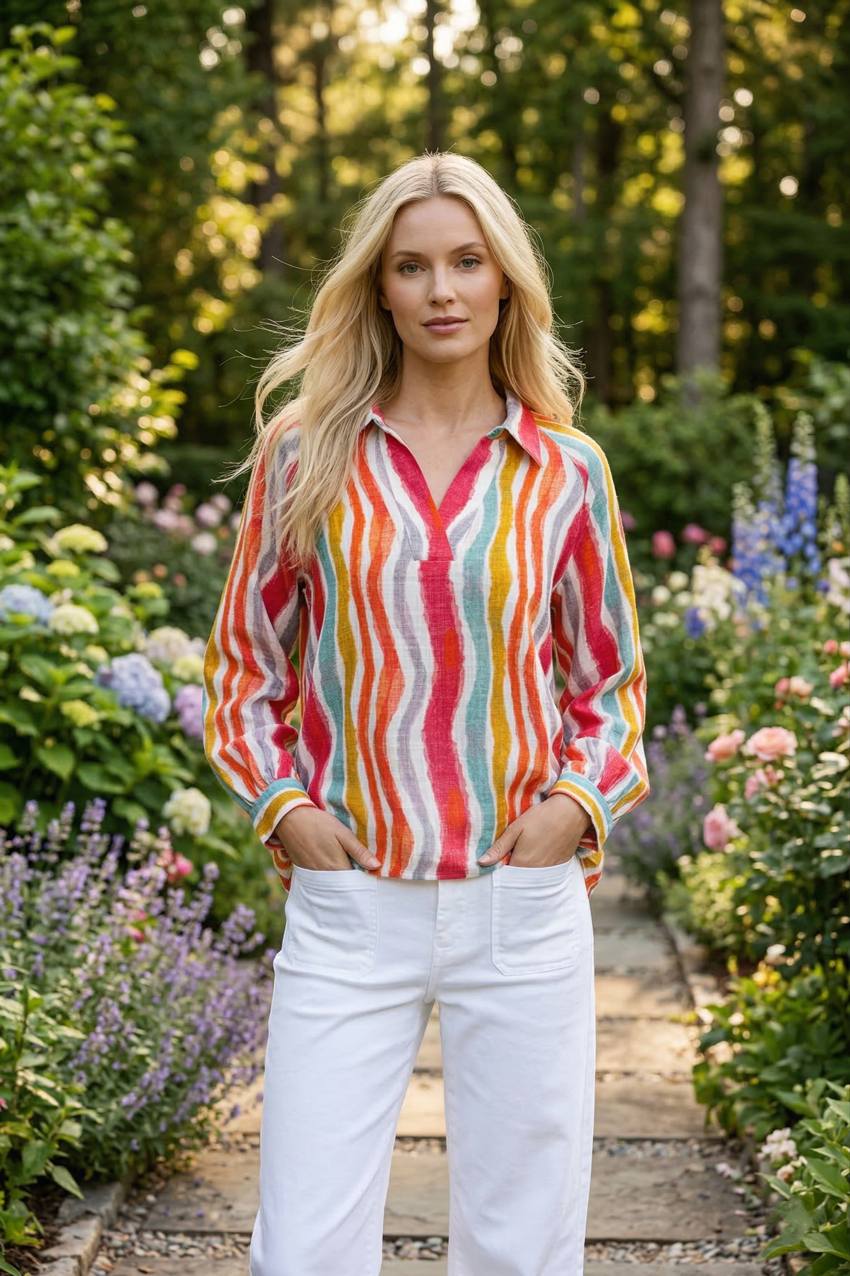 Woman in a colorful striped shirt and white pants standing in a garden.