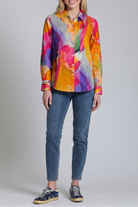 Person wearing a colorful patterned shirt and jeans on a plain background