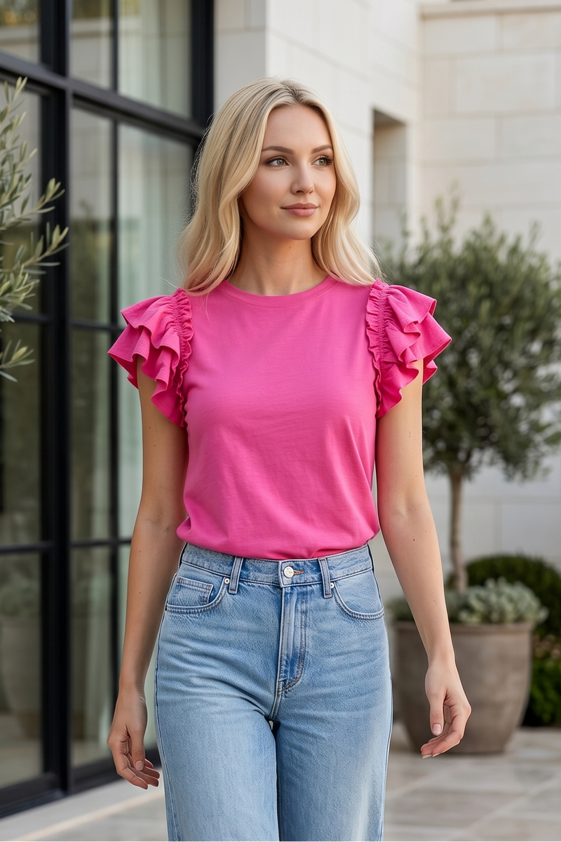 Woman wearing a pink top with ruffled sleeves and blue jeans standing outdoors.