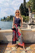 Woman in a colorful dress standing by a scenic lakeside with statues and trees.